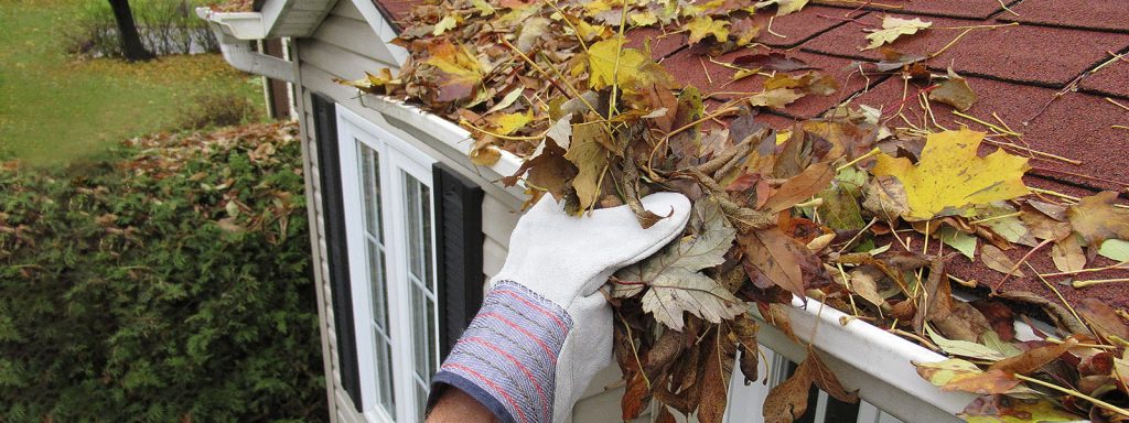 A homeowner cleans a gutter full of leaves