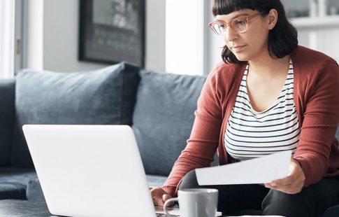 Woman looking at laptop on coffee table and holding a tax document