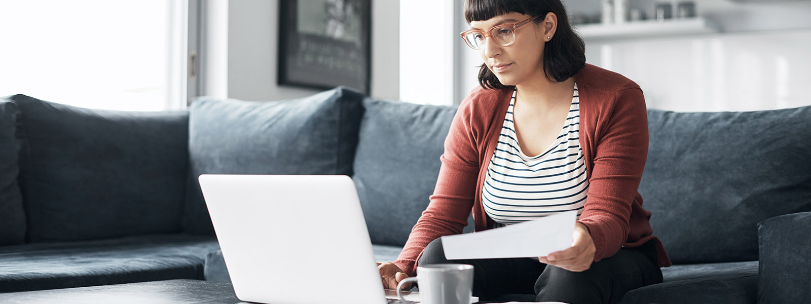Woman looking at laptop on coffee table and holding a tax document