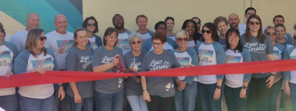 Group of men and women pose for a picture at a ribbon cutting