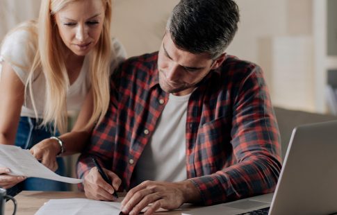 Man and woman looking at paperwork by a laptop, discussing reasons for a rejected home offer