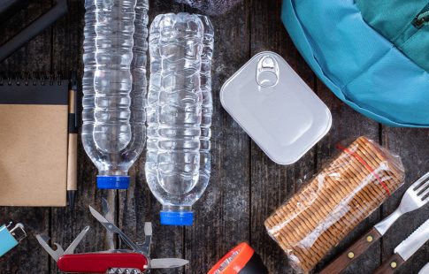 A group of home emergency survival kit supplies including water bottles, canned food, a radio, band-aids, and batteries