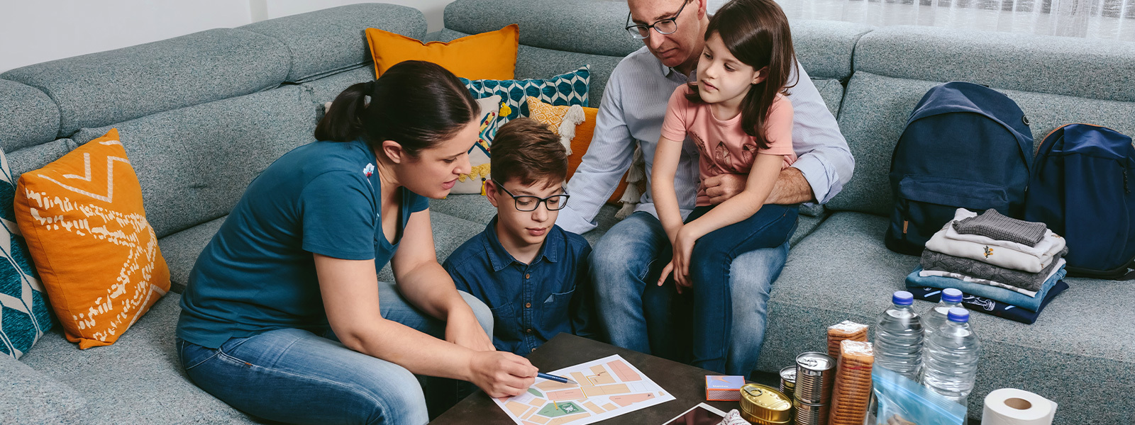 Family sitting in a living room with natural disaster supplies