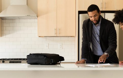 A male real estate agent discussing paperwork with a woman at a kitchen island.