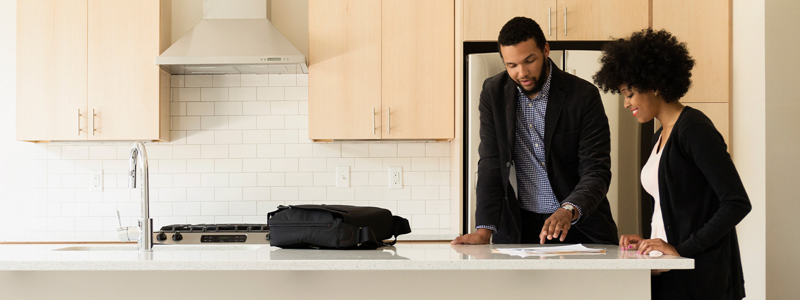 A male real estate agent discussing paperwork with a woman at a kitchen island.