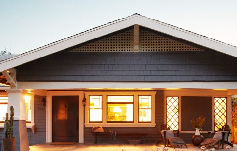 Blue bungalow house with interior lights on in early evening.