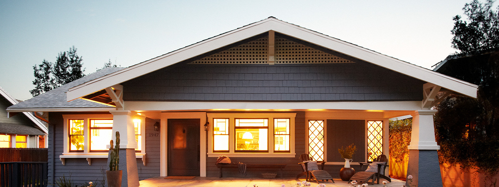 Blue bungalow house with interior lights on in early evening.