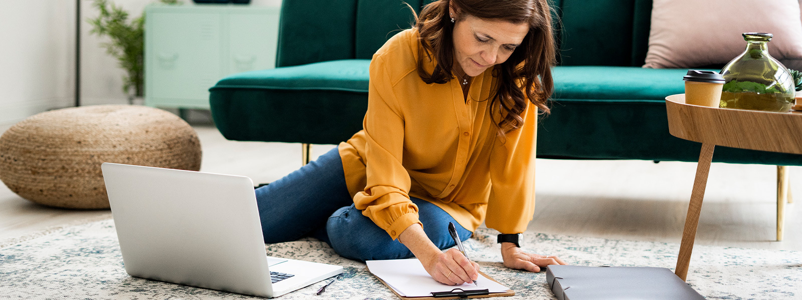 Woman sitting on the floor with a laptop, checklist, and binder of paperwork