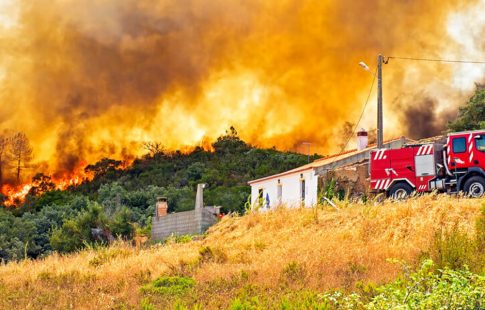 Wildfire burning in hills behind a building and commercial truck