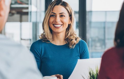 Woman at a desk holding a piece of paper, smiling at man and woman sitting across from her