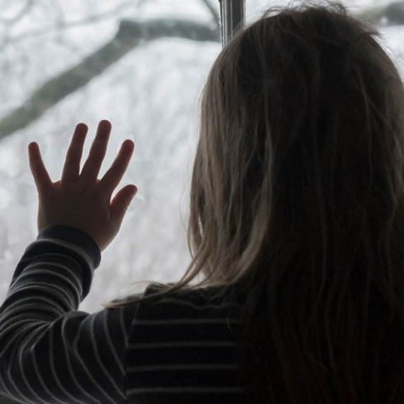 Girl looking out a window on snow-covered trees