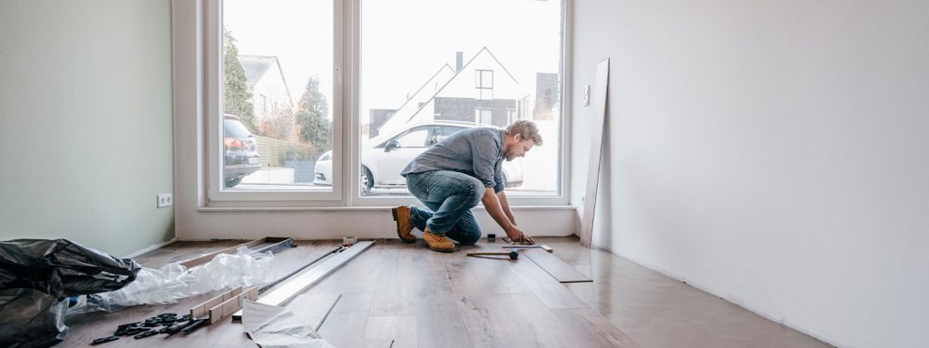 Man installing laminate wood flooring to add value to his home.