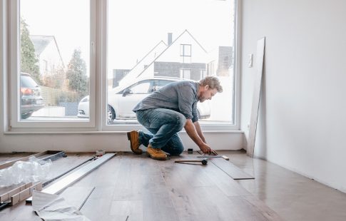 Man installing laminate wood flooring to add value to his home.