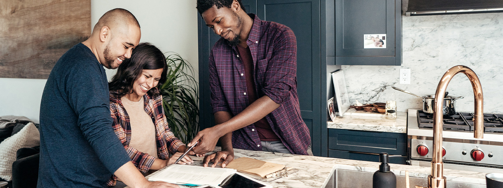 A couple looks at paperwork in a kitchen with a real estate agent. Finding an agent who works in the area where you plan to buy a home is an item that can be added to a buying a home checklist.