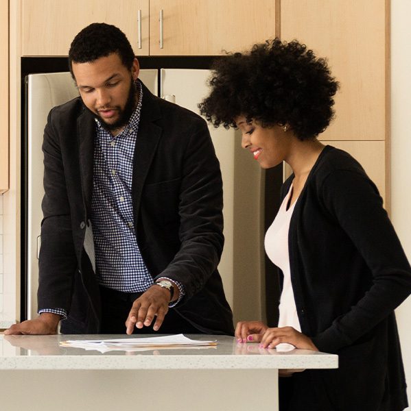 A male real estate agent discussing paperwork with a woman at a kitchen island.