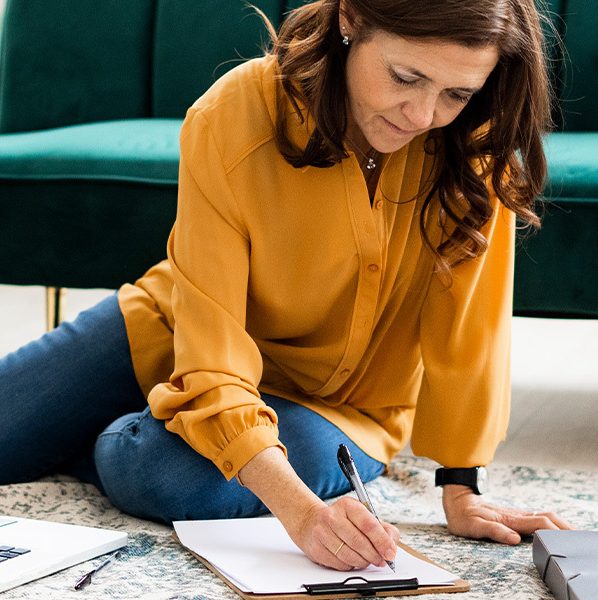 Woman sitting on the floor with a laptop, checklist, and binder of paperwork