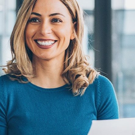 Woman at a desk holding a piece of paper, smiling at man and woman sitting across from her