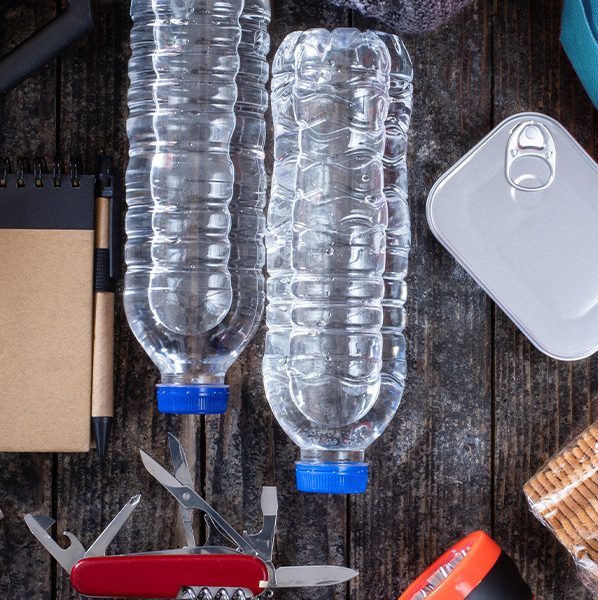 A group of home emergency survival kit supplies including water bottles, canned food, a radio, band-aids, and batteries