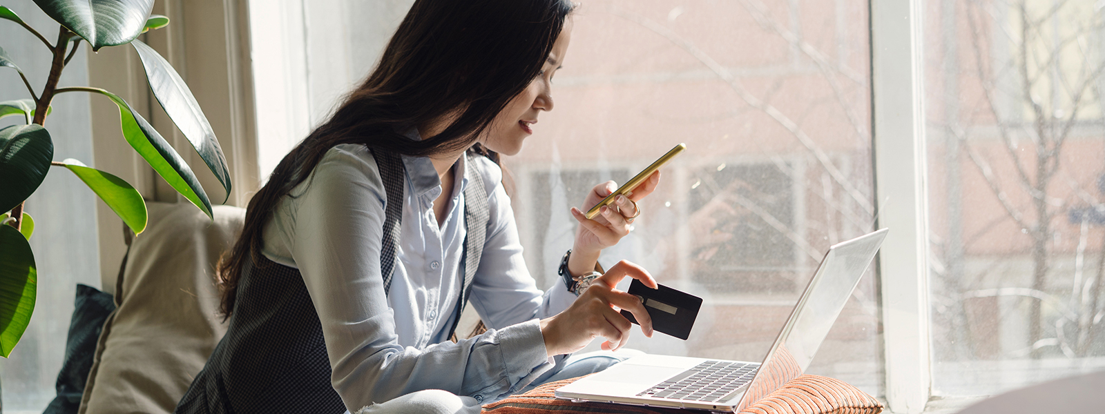 Woman holding credit card and smart phone in front of laptop, wondering, "can you consolidate credit card debt into your mortgage?"