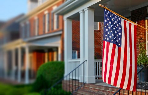 U.S. flag hanging from the front porch of a brick house; lead image for article on facts about va loans