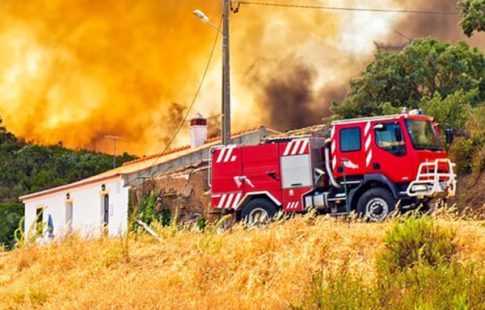 Wildfire burning in hills behind a building and commercial truck