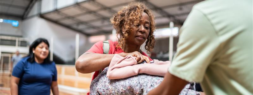 Woman receiving blankets from a volunteer in a temporary shelter in a gym
